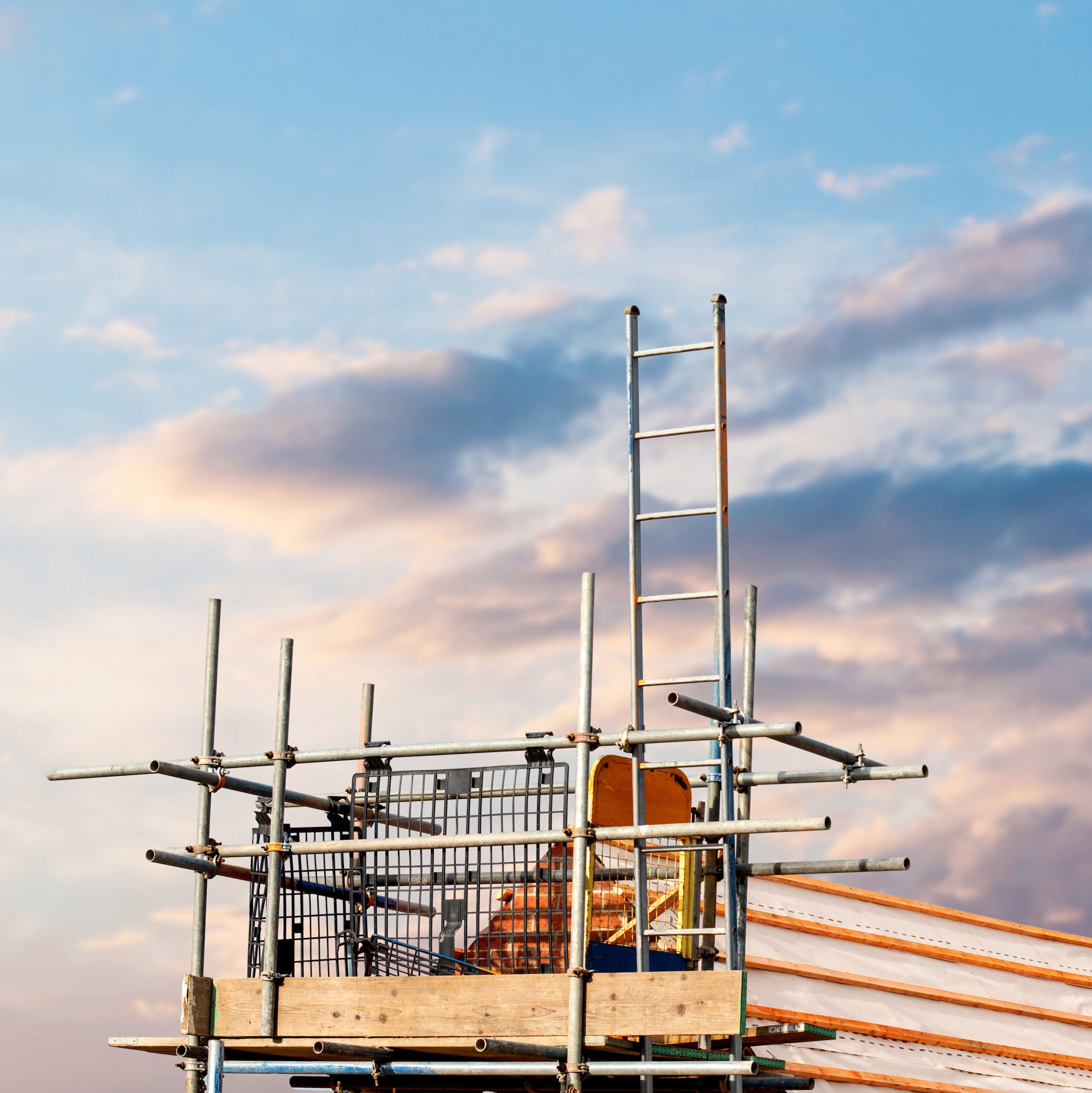 Construction site with a house being built from brick and timber, featuring brickwork, roof trusses and scaffolding. House roof construction in progress